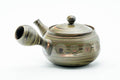 Side profile of the teapot, spout to the left and hollow side handle facing the viewer.
