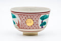 Three-quarter front view of the cream chawan painted with pink geometric lattice and green pine motifs in akae enamel