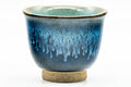 Close-up of a single blue cup, three-quarter view of the turquoise glaze dripping down the body.