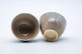The two cups tipped to reveal their glazed interiors and unglazed feet.