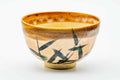 Peach-glazed Karatsu-yaki matcha bowl, three-quarter view, painted with green long-grass brushwork and an iron-brown rim.
