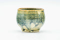 Small yunomi teacup in green and yellow hare's-fur drip glaze, front view.