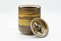 Three-quarter view of the mizusashi with its flat ceramic lid removed and propped upright beside the container.