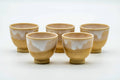 The set of small Hagi-yaki cups grouped together, showing their beige-and-white drip glaze.