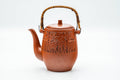 Front view of a tall red shudei Tokoname-yaki dobin (top-handled teapot) with an arched handle and engraved Egyptian-style motifs, lid on, spout to the left.
