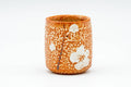 Single orange Shino yunomi teacup, front view, mottled orange glaze with white plum-blossom motifs.