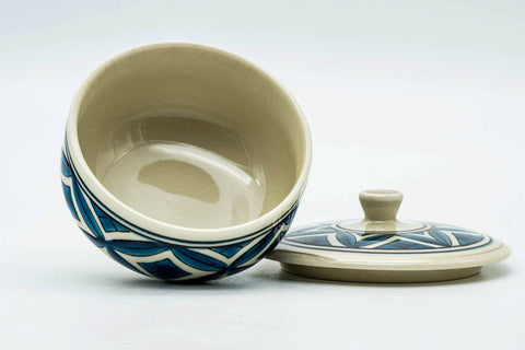 The teacup tipped to show the interior, with the lid set beside it.