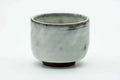 Small teacup with a milky white crackle glaze and a darker rim, front view.