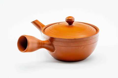 Side view of the wide red kyusu with the handle to the left, lid on.