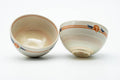 A pair of cream Kyo-yaki yunomi with striped rim bands, one tipped to show a small painted motif inside.