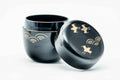 Black-lacquer matcha tea caddy (natsume) with gold geometric soaring-bird maki-e, lid removed and lying beside the upright body, three-quarter view