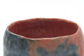 Side view of the chawan highlighting the mottled red and grey raku glaze and incurving wall.