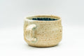 Side view of the handled teacup, sandy speckled stoneware body with a single side handle.