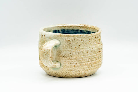 Side view of the handled teacup, sandy speckled stoneware body with a single side handle.