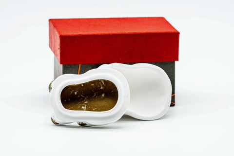 Three-quarter view with the dog's upper body lifted off as a lid, revealing the hollow interior with gold detail, beside the box.