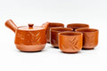 Red-orange Tokoname-yaki side-handle kyusu shown with its matching yunomi teacups, three-quarter view with engraved bamboo motif and lid in place.