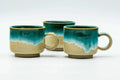 The three cups from another angle, showing the turquoise drip glaze.