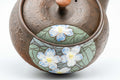 Three-quarter view highlighting the painted white lily panel on the textured body.