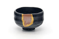 Black raku-yaki matcha bowl (chawan) with red-brown patches and a gold kintsugi repair seam, three-quarter view