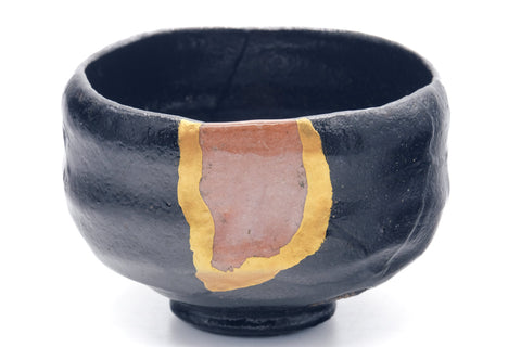 Black raku kintsugi chawan, three-quarter view highlighting the prominent gold kintsugi seam down the body