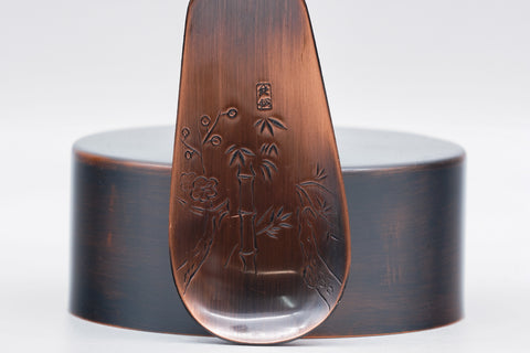Top-down view of the canister lid and the engraved floral tea scoop.