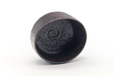 The chawan tilted to show its dark interior with a spiral mark.