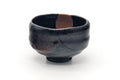 Black raku kintsugi chawan, front view showing the dark glaze, warm red areas and a vertical gold repair line