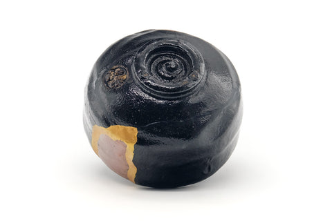 Black raku kintsugi chawan inverted to show the underside and foot ring with gold repair extending toward the base